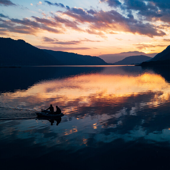 Blick auf den Ossiacher See und auf ein Schifferboot mit 2 Herren zur blauen Stunde.